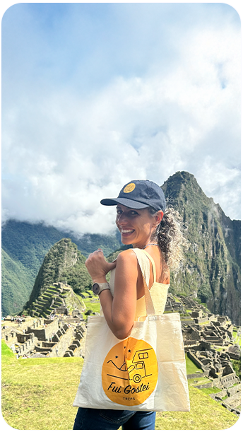 Carla, da Fui Gostei Trips, sorrindo em Machu Picchu com bolsa e boné da agência, durante passeio em Cusco, Peru.