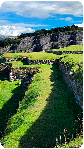 Ruínas do sítio arqueológico de Sacsayhuamán em Cusco, Peru, com muros de pedra impressionantes e gramado verde sob céu azul — parada imperdível nos roteiros dos passeios de cusco da Fui Gostei Trips.