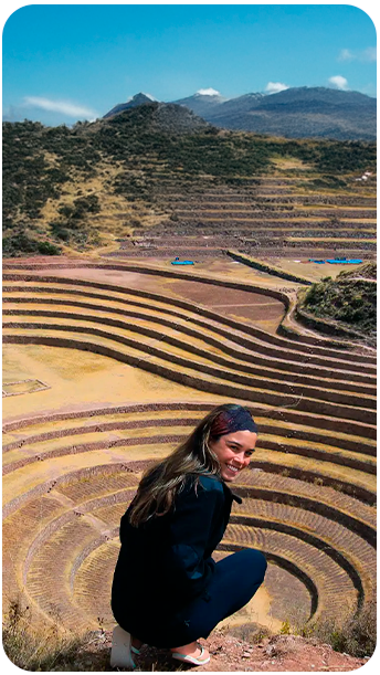 Turista sorridente no impressionante sítio arqueológico de Moray, em Cusco, com seus terraços circulares incas usados para experimentos agrícolas — uma das paradas culturais da Fui Gostei Trips no Peru.