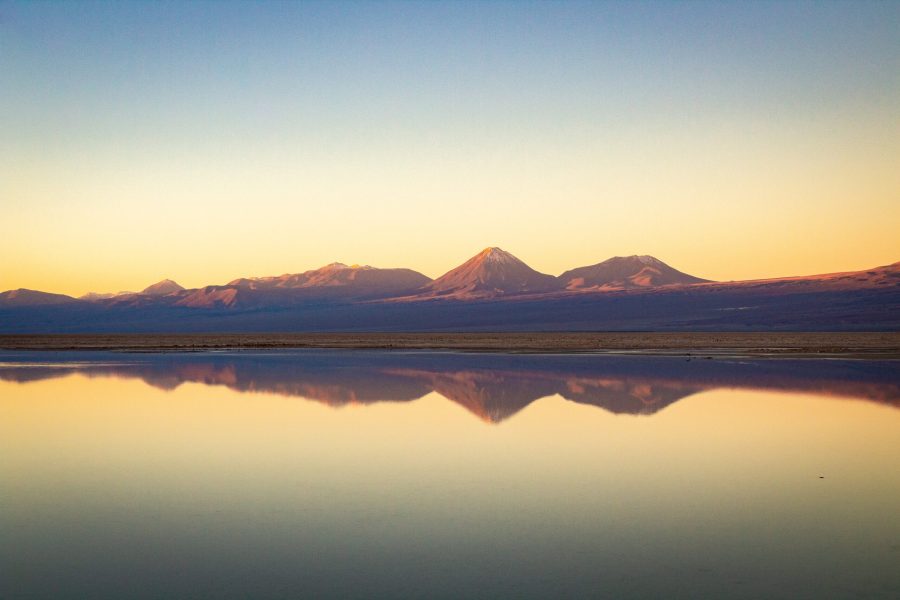 imagem do atacama, com um grande lago espelhado, montanhas ao fundo e sol se pondo
