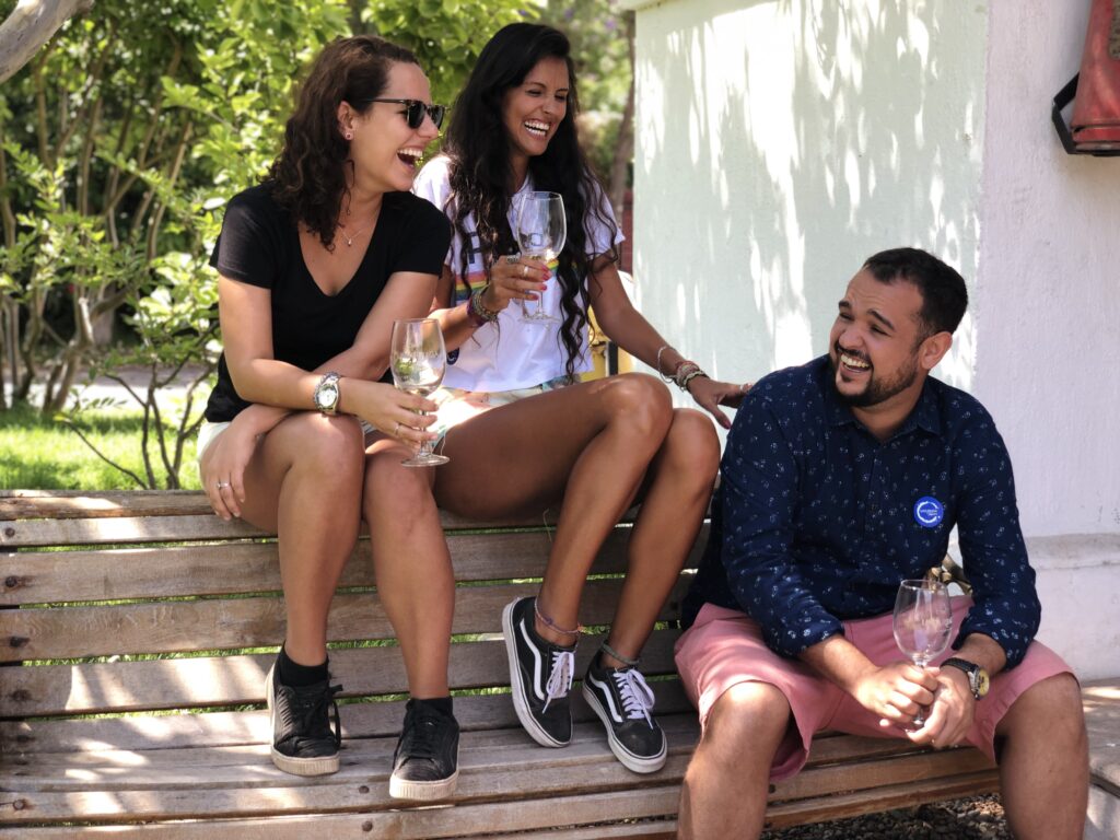 Grupo de três pessoas sentados em um banco sorrindo com taças de vinho na vinícola Undurraga no Chile