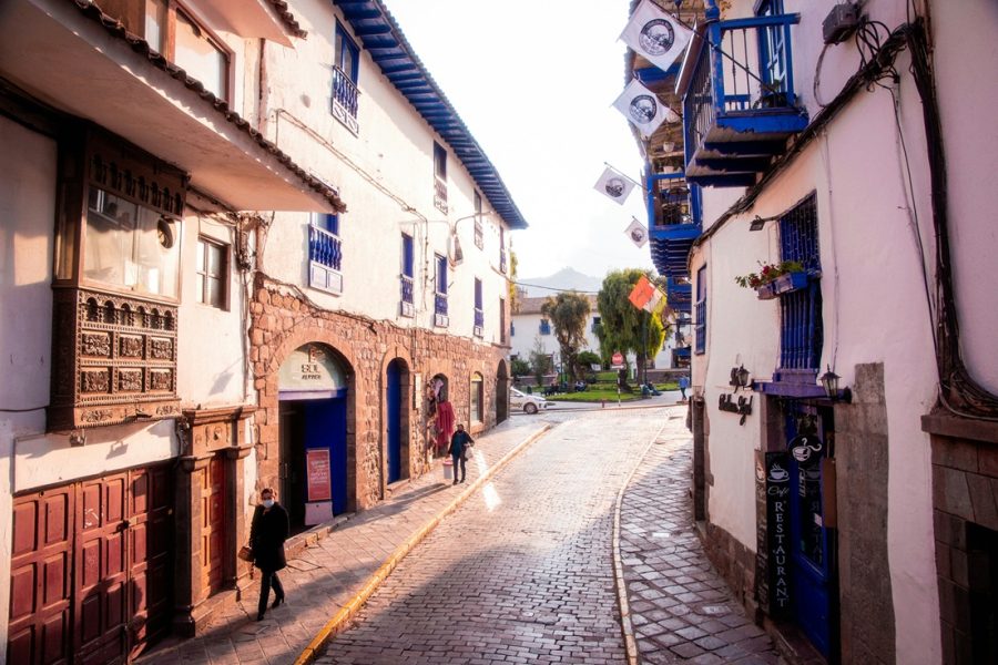 Rua de Cusco com paralelepípedo, casa pintada de branco, bancadas azuis.