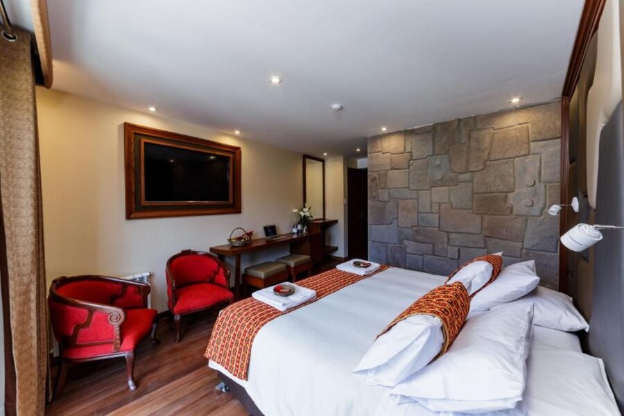 Vista de trás de uma cama casal em Cusco, em um quarto com uma televisão, móveis e poltronas