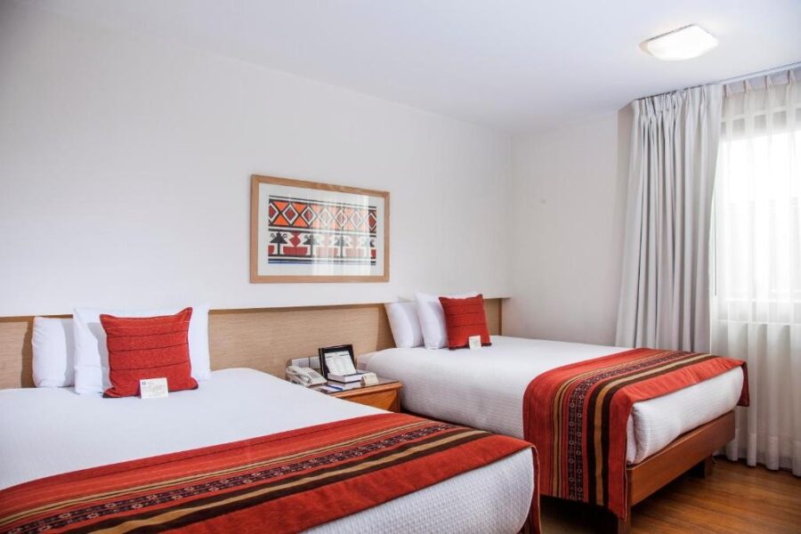 quarto branco com duas camas, um quadro na parede e uma janela para a varanda com cortina
