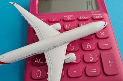 Imagem com avião branco com asas em detalhes vermelho, pousando em cima de uma calculadora simples vermelha, simbolizando o planejamento financeiro para viagens.
