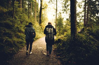 imagem mostra duas pessoas caminhando numa trilha em meio à floresta, simulando a prática do ecoturismo e turismo responsável