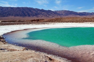foto demonstrativa da rota dos salares , um dos principais roteiros no deserto do atacama. A imagem mostra uma cena de dia da área composta por lagoa salgada e montanhas ao fundo