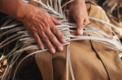 imagem mostra duas mãos produzindo artesanato com palhas secas, demonstrando a produção local das comundiades em áreas turísticas