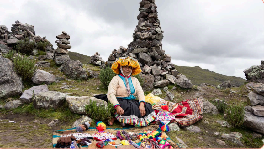 Mulher com roupa colorida sentada em meio a pedras em formato de esculturas, no topo de uma montanha