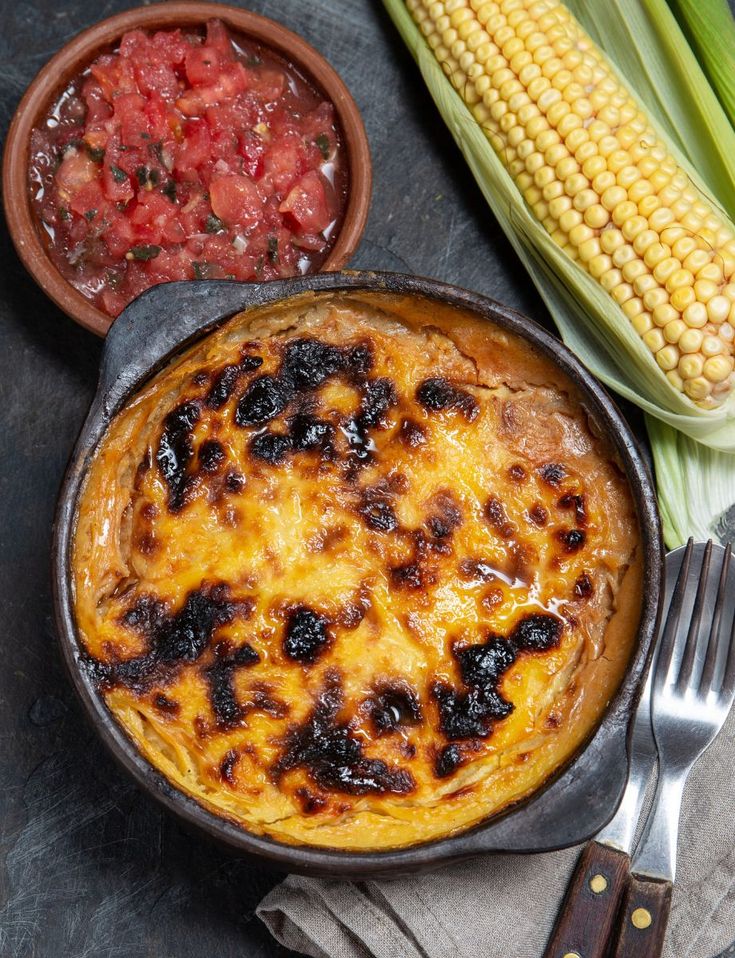 O prato é típico de restaurantes bons e baratos do Chile, pastel de choclo. A imagem contem o prato sobre uma bancada preta com um garfo ao lado e um milho e espiga.