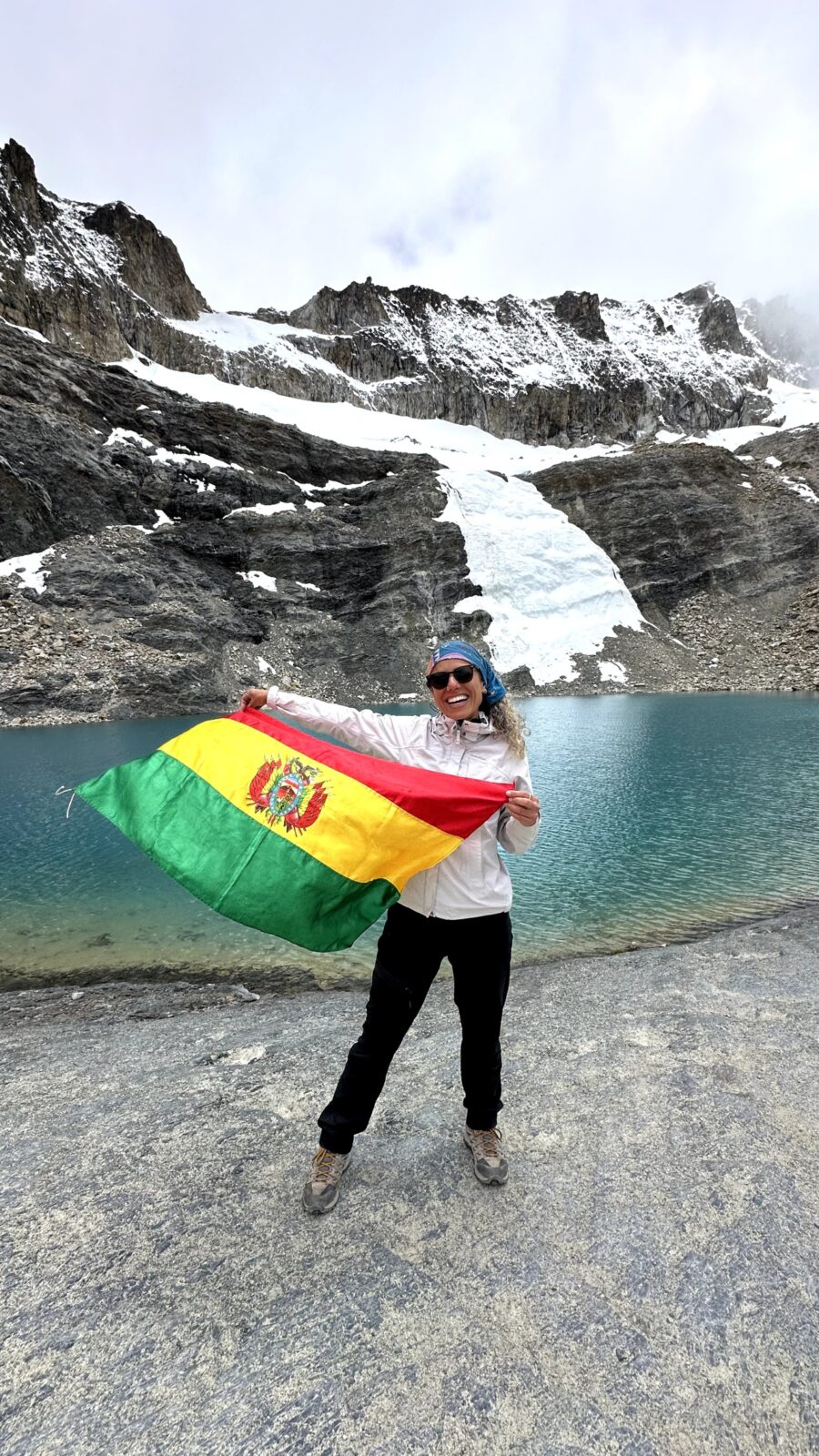turista segurando a bandeira da bolívia no pé de um rio na montanha nevada em la paz