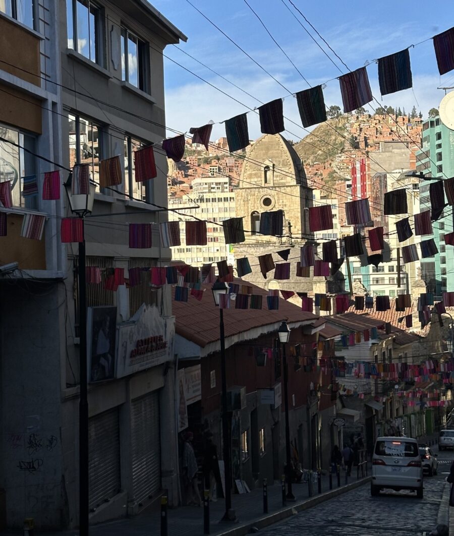 imagem de uma rua em la paz com várias bandeiras hasteadas, predios nas calçadas e dia claro