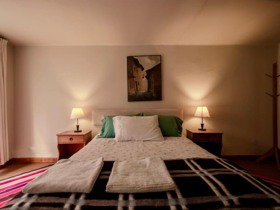 quarto com um quadro, cama coberta e abajures nas laterais