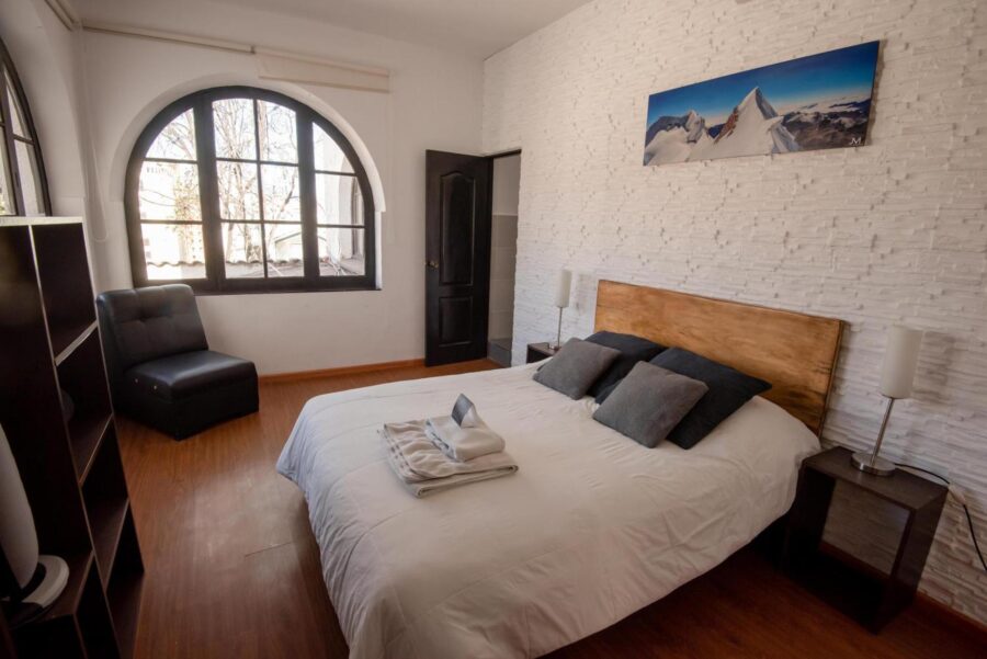 quarto com uma janela em meio arco, uma cama coberta e piso de madeira