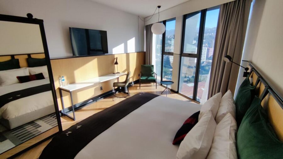 quarto com uma grande janela para a cidade, uma cama de frente para uma tv e um movel