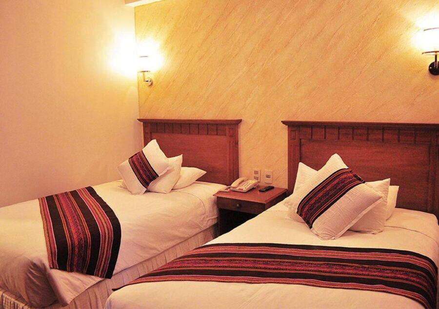 quarto com um abajur de parede ligado e duas camas de solteiro