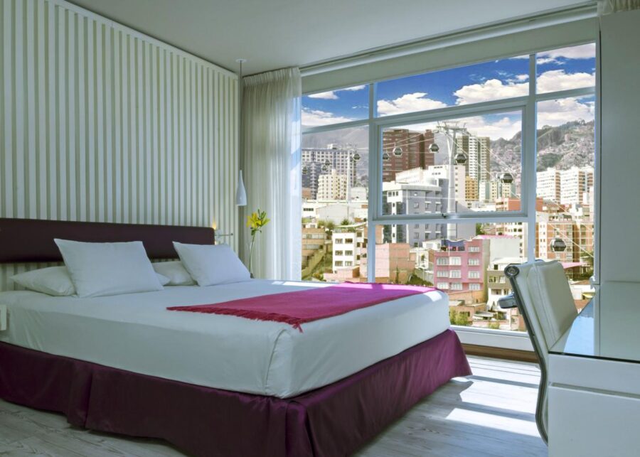 quarto com uma cama com colcha roxa e uma grande janela olhando para a cidade