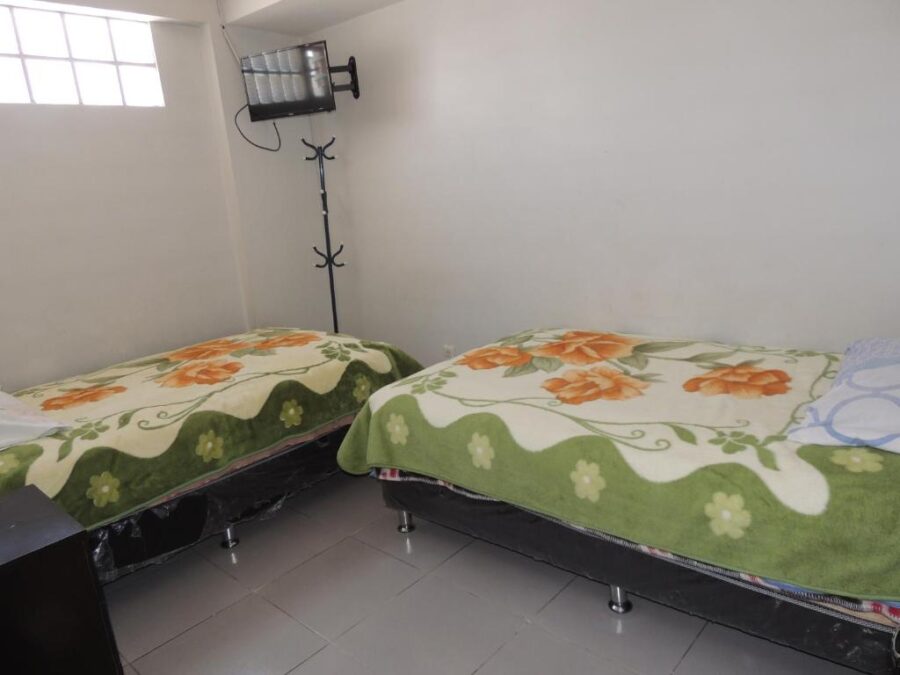 quarto com duas camas cobertas, uma pequena janela ao fundo e uma televisão