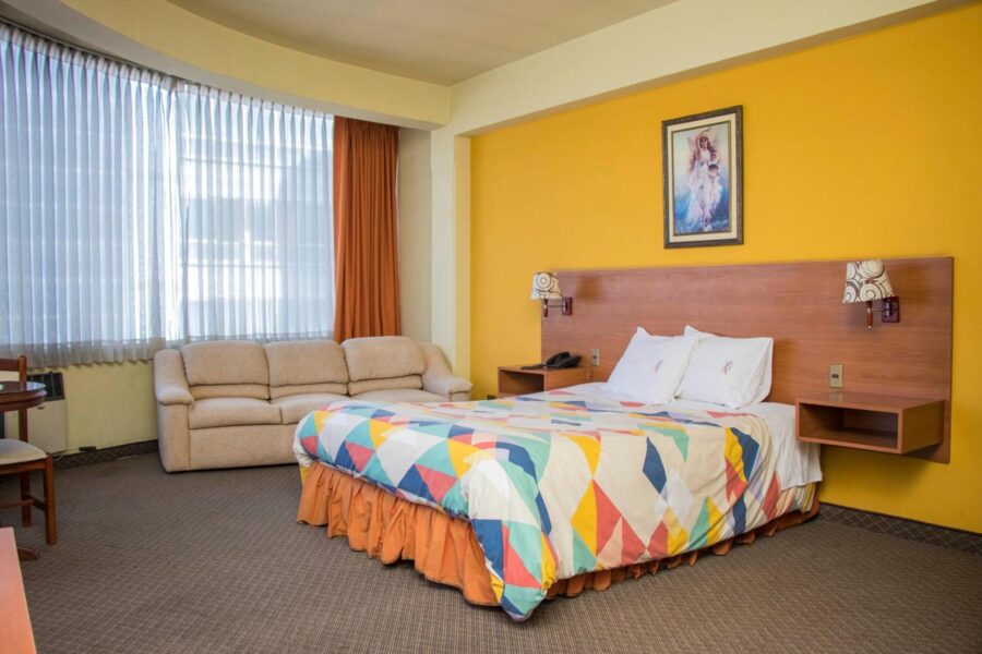 quarto com uma parede amarela, carpete, sofa proximo a janela e uma cama casal