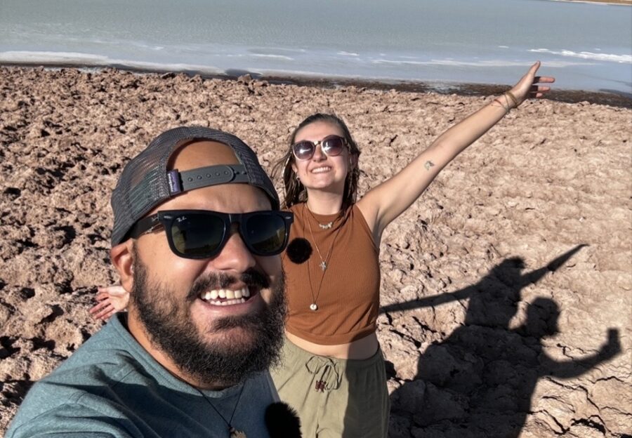 Casal sorrindo em selfie no Deserto do Atacama, aproveitando paisagem árida e lagoa em viagem de lua de mel