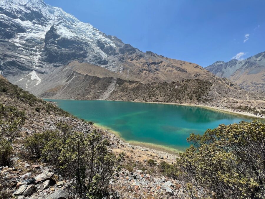 Vista da Laguna Humantay com águas turquesa cristalinas cercadas por montanhas rochosas e picos nevados sob céu azul