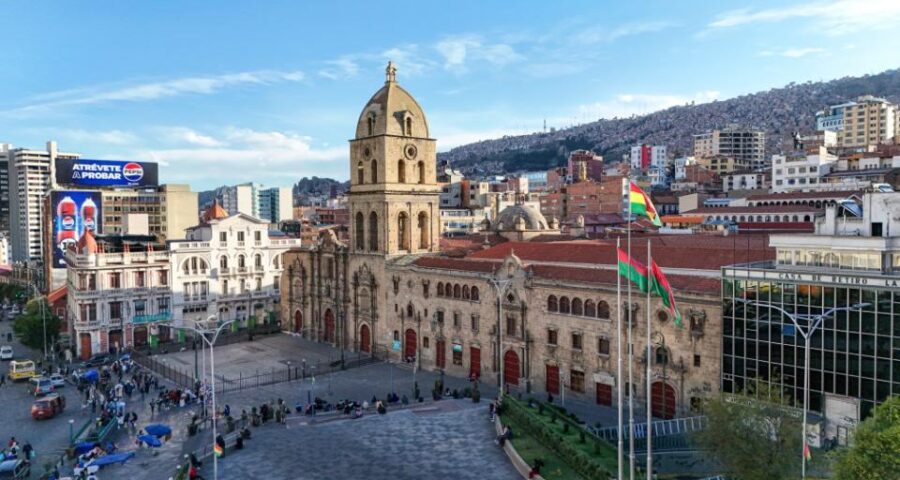 Praça central de La Paz com igreja histórica, prédios ao redor e pessoas caminhando. Cenário encantador para lua de mel em La Paz