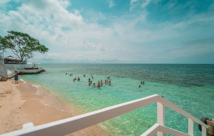 Praia de águas cristalinas em Cartagena, com pessoas nadando no mar do Caribe e vista a partir de um deck à beira-mar.