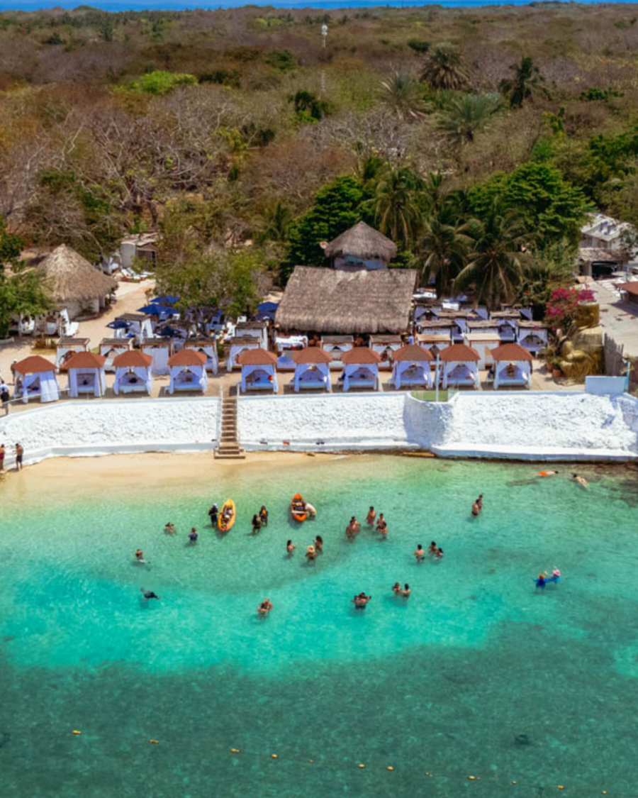 Vista aérea de praia em Cartagena com águas azul-turquesa, pessoas no mar e estrutura de beach club à beira da praia.
