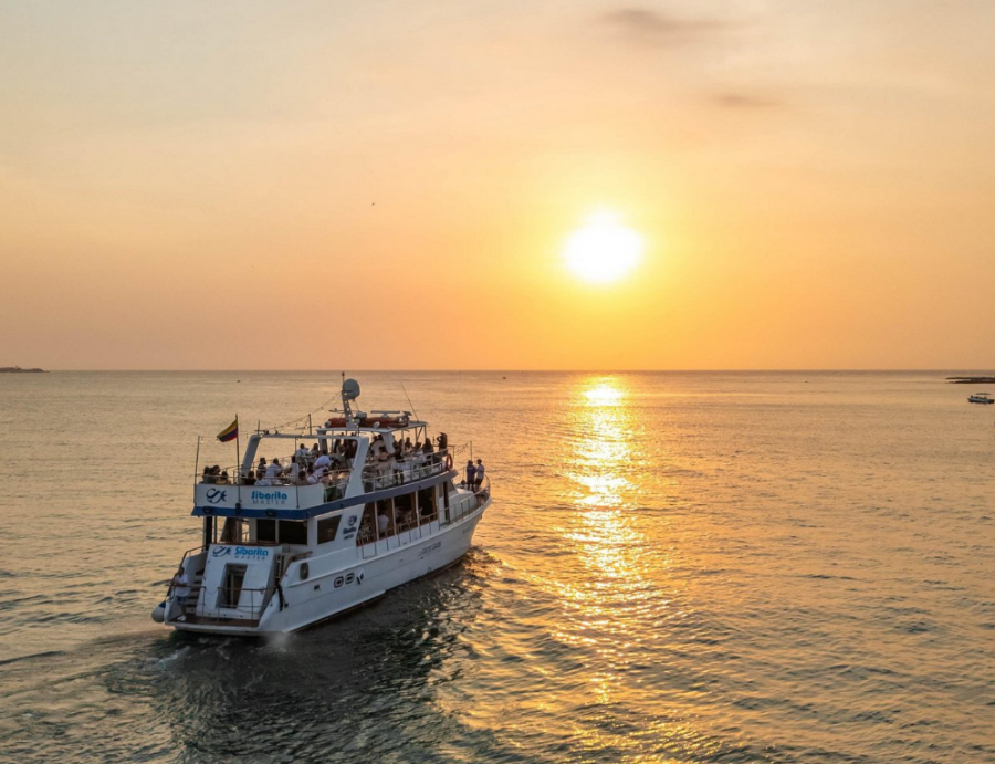 Barco navegando ao pôr do sol em Passeio em Cartagena, na Baía, com céu alaranjado e reflexo dourado no mar.
