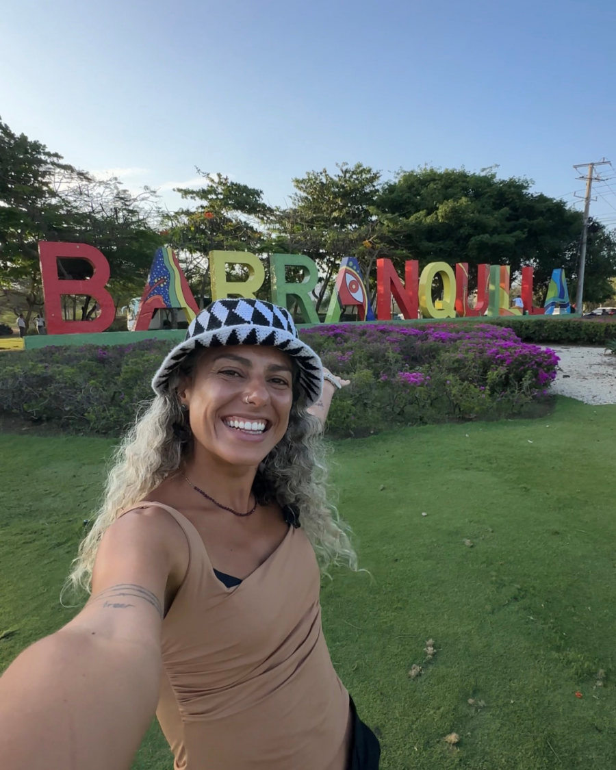 Mulher sorrindo em frente ao letreiro colorido de Barú, em Cartagena, durante um passeio ao ar livre em área turística com jardins e vegetação tropical.