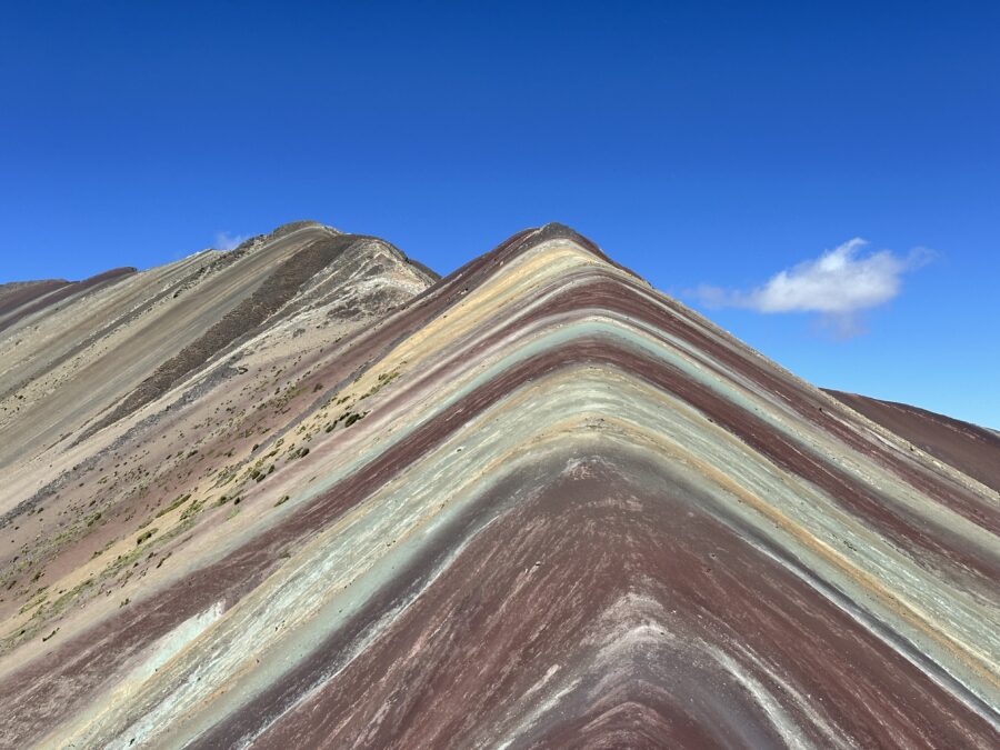 Montanha com faixas coloridas em tons de vermelho, verde e bege sob céu azul, cenário lindo para lua de mel em Cusco e Machu Picchu
