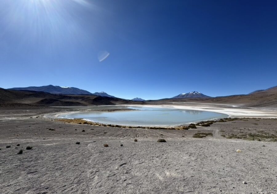 Lagoa cercada por paisagem desértica no Salar de Uyuni, com montanhas ao fundo e céu azul limpo