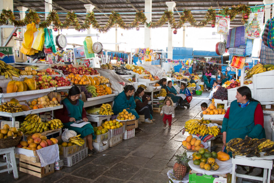 Interior do Mercado de San Pedro, em Cusco, com bancas de frutas frescas e vendedores locais.