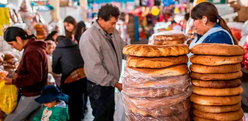 Bancas de pães tradicionais no Mercado de San Pedro, em Cusco, com visitantes circulando pelo local.