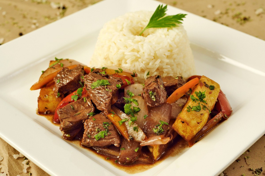 Prato de lomo saltado peruano com pedaços de carne, legumes salteados, batatas douradas e arroz branco.