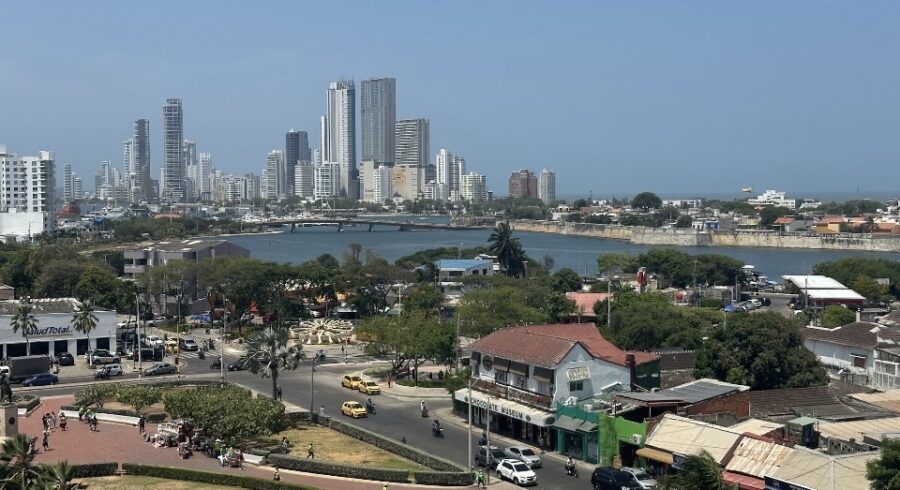 Vista panorâmica de Cartagena com prédios modernos ao fundo, canal de água, ruas movimentadas e área urbana observada de um ponto elevado da cidade.