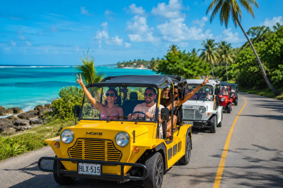 Grupo de turistas passeando de mule pela estrada costeira de San Andrés, com o mar de sete cores ao fundo, coqueiros à beira da pista e céu azul ensolarado, em uma típica volta à ilha pelo Caribe colombiano.