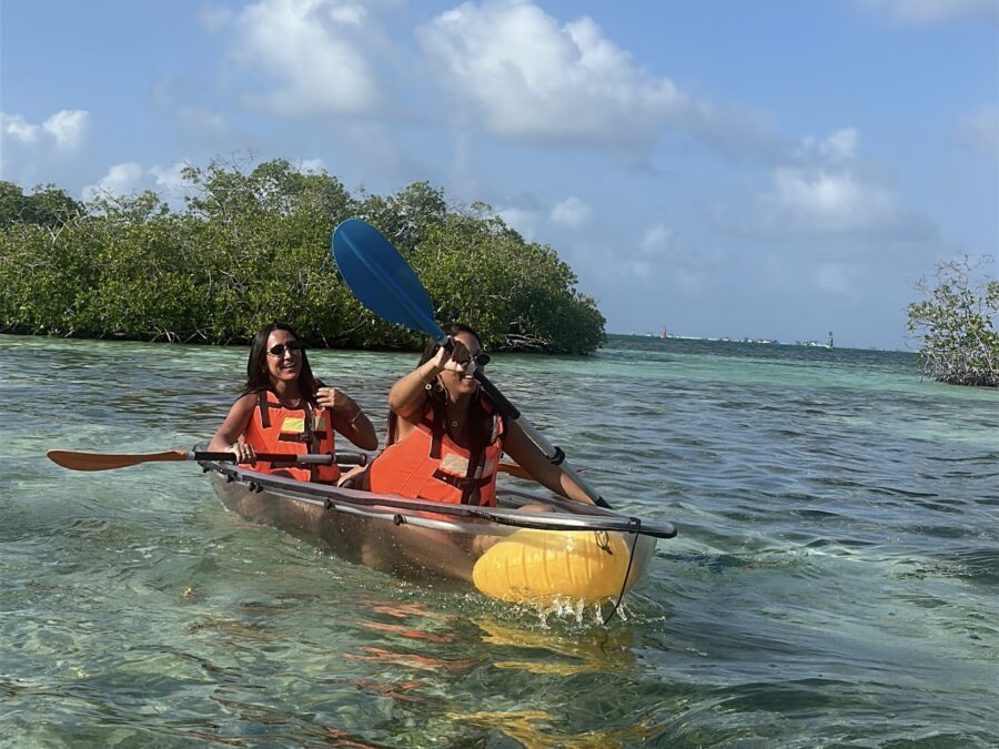 Duas pessoas em um caiaque transparente navegando por águas cristalinas na melhor época para ir para San Andrés, cercadas por manguezais e paisagens tropicais.