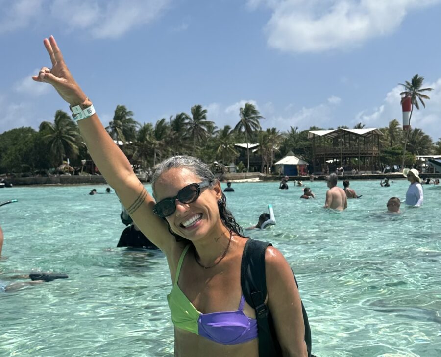 Mulher em praia ensolarada, sorrindo com óculos de sol, em viagem que incluiu a Tarjeta do Turismo em San Andrés