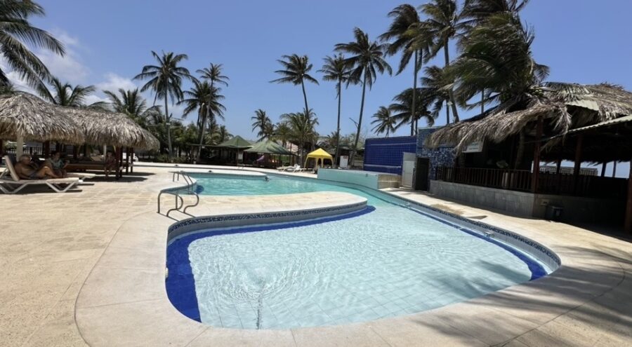 Piscina com coqueiros e quiosques de palha no Caribe colombiano, inspiração de hospedagem para quem busca o que fazer em Cartagena e arredores.