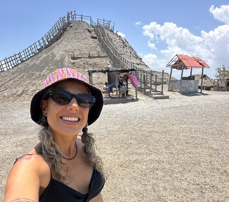 Cartagena ou San Andrés: Mulher sorrindo em frente ao Vulcão do Totumo, próximo a Cartagena, usando chapéu e óculos de sol, com a escadaria de acesso ao vulcão ao fundo em um dia de céu azul. A imagem ilustra o que fazer em Cartagena, incluindo um dos passeios mais populares nos arredores da cidade