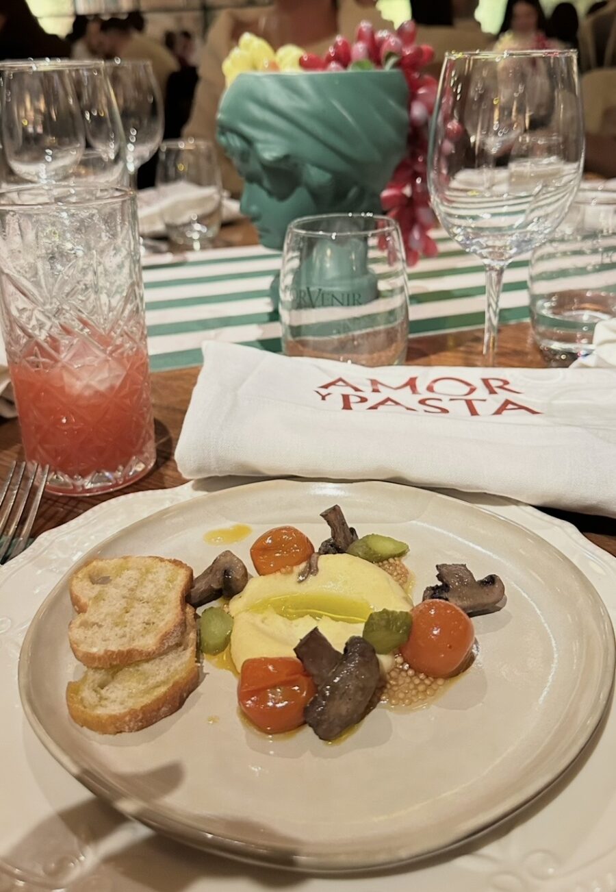 Prato preparado no Amor e Pasta, mostrando massa coberta por tomates e folhas, acompanhado por bebida