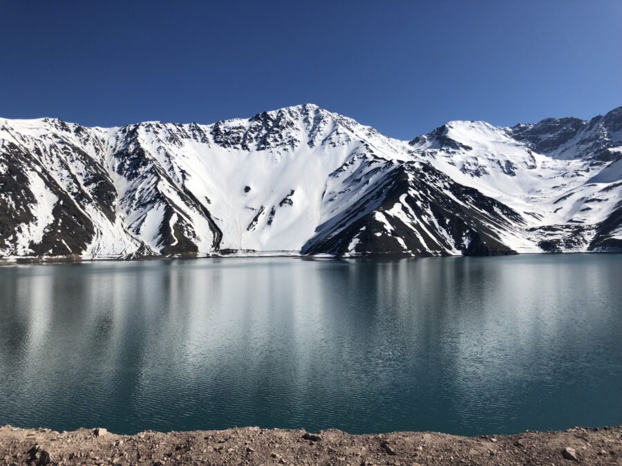 Lago de montanha cercado por picos nevados nos Andes chilenos. Possibilidade de viagem a Santiago em 2027