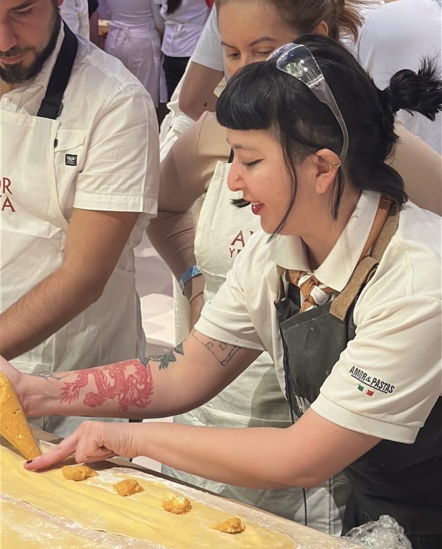 Pessoa preparando massa artesanal em uma experiência gastronômica da Amor e Pasta, com raviolis sendo montados sobre uma bancada enfarinhada