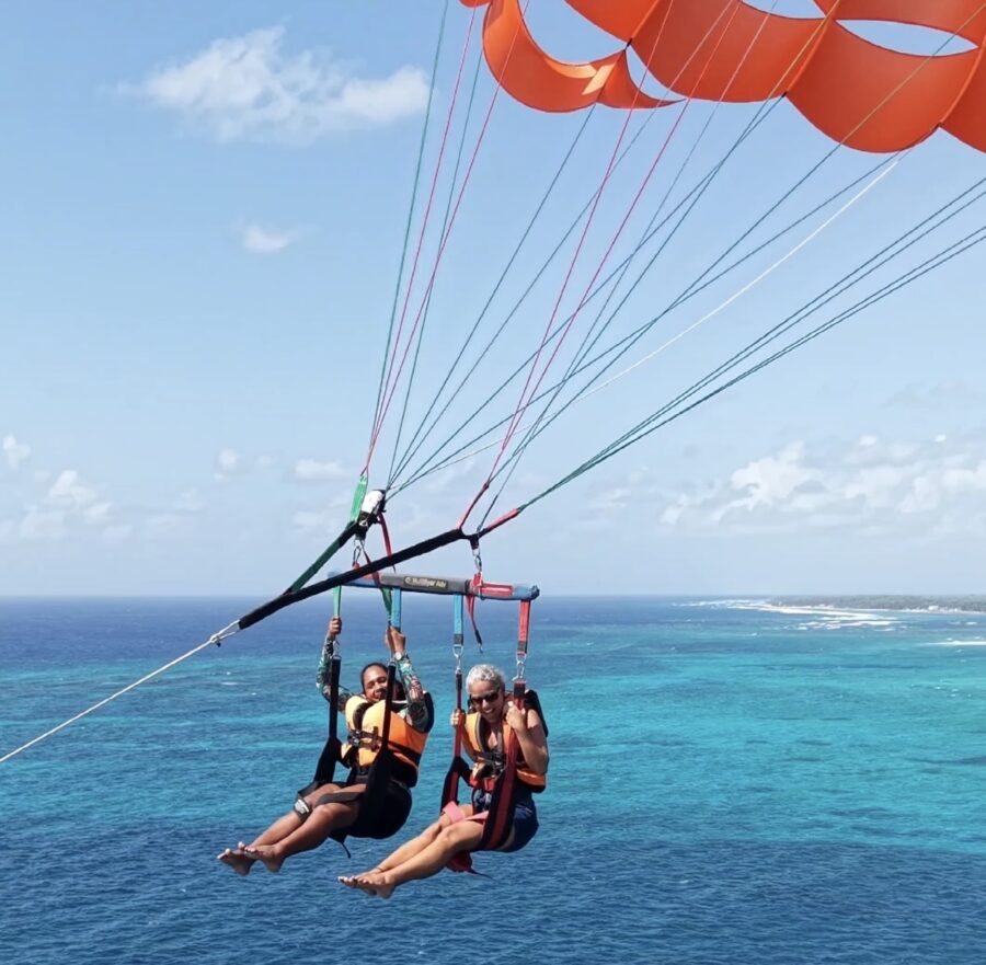 Parasail em San Andrés com duas pessoas voando sobre o mar de sete cores e um paraquedas laranja ao fundo