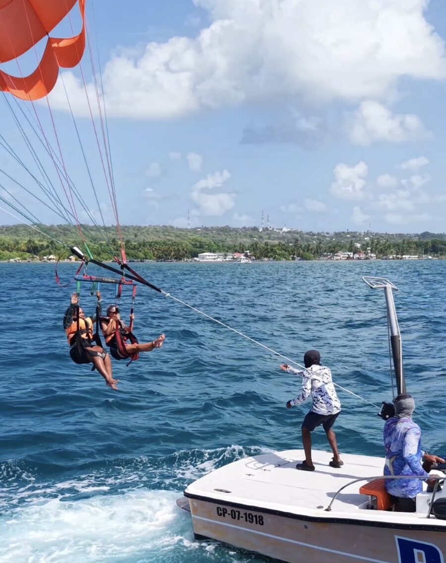Parasail em San Andrés com duas pessoas sendo suspensas sobre o mar azul-turquesa e puxadas por uma lancha, usando equipamentos de segurança