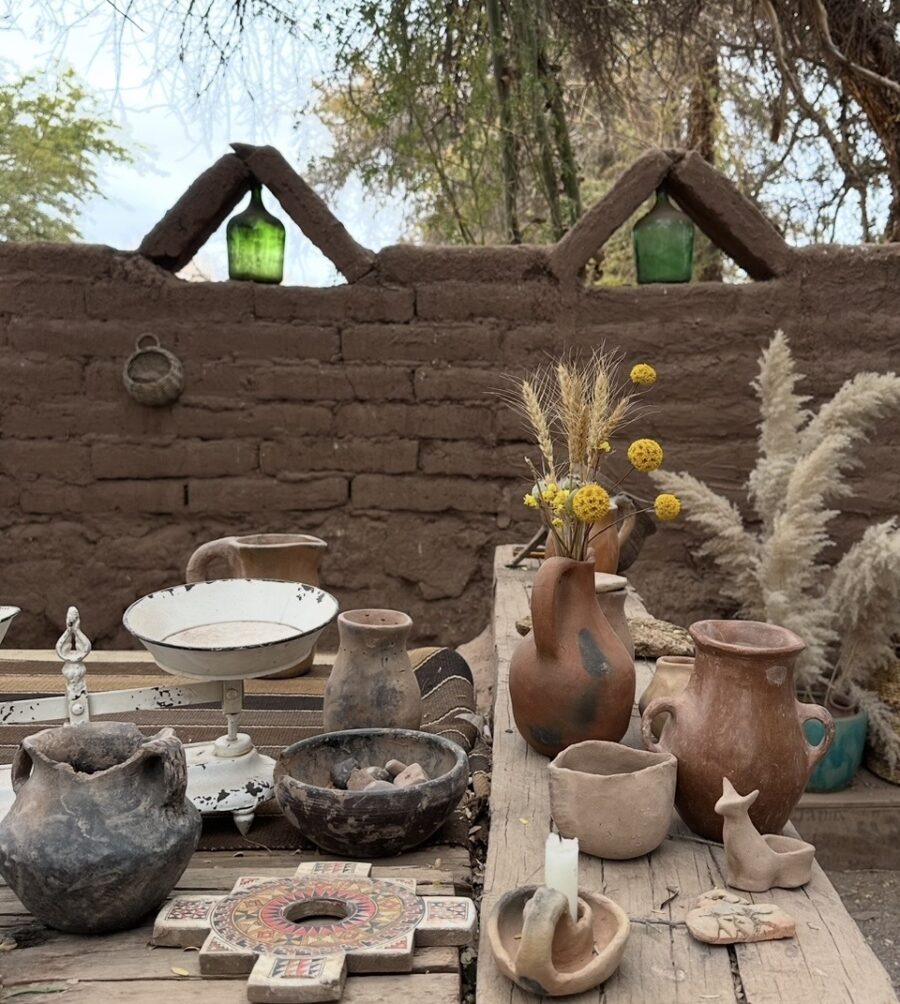 Mesa rústica com cerâmicas artesanais, utensílios de barro e flores secas em um espaço tradicional da experiência Atacama Ancestral, destacando elementos da cultura e das tradições do Deserto do Atacama