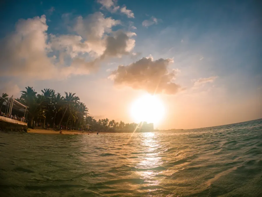 Noche Blanca ou Yate Rumba; Pôr do sol dourado sobre o oceano, visto do nível da água próximo a uma praia com palmeiras em San Andrés