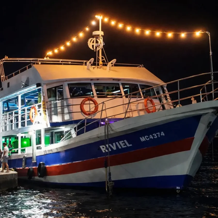 Noche Blanca ou Yate Rumba em San Andrés: Close-up de um barco de dois andares decorado com luzes de corda, atracado à noite.