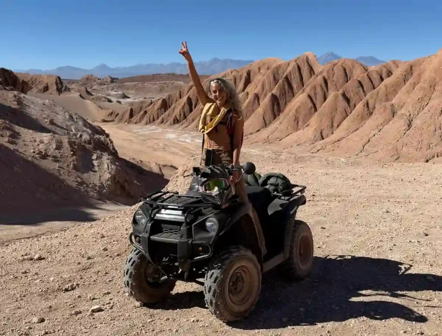 Mulher em quadriciclo em um dia ensolarado no Atacama, sorrindo com os braços erguidos e paisagem desértica ao fundo. Possibilidade de onde viajar no Ano Novo 2026 ou no Natal